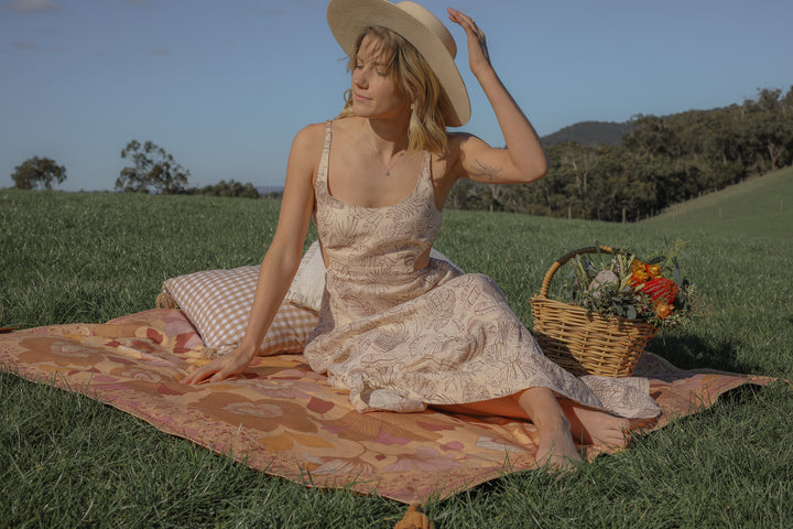 Girl in boho linen maxi dress with tropical print having a picnic in green field with flowers and wine.