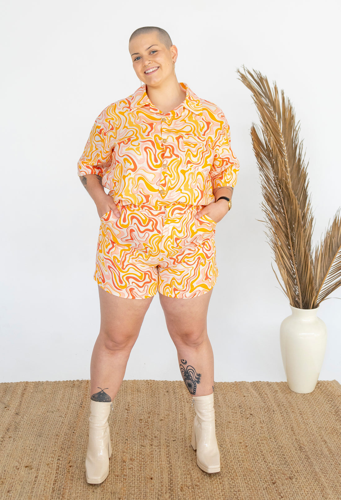 girl wearing boho 70's inspired linen shirt and shorts set. styled with white go go boots, a rattan chair and dried palm leaves.